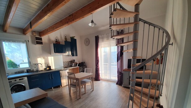 A modern kitchen with blue cabinets, a dining area with a table and chairs, a sofa, and a spiral staircase. - Duplex Nights & Days in Nuits-Saint-Georges (Nuits-Saint-Georges)
