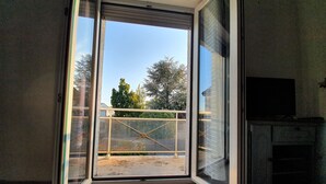 A room with a sliding glass door leading to a balcony with a metal railing and a view of trees and a building. - Duplex Nights & Days in Nuits-Saint-Georges (Nuits-Saint-Georges)