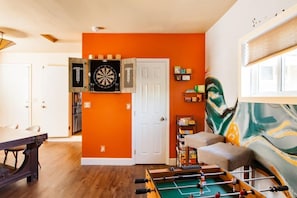 A room with a dartboard, foosball table, and a sofa.