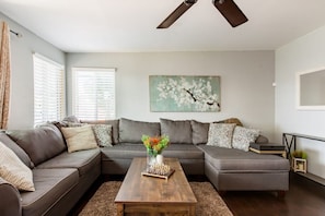 A living room with a sectional sofa, a coffee table, and a painting on the wall.