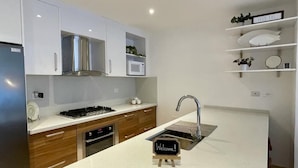 Een moderne keuken met witte kastjes, een roestvrijstalen afzuigkap, een ingebouwde magnetron en een spoelbak met een 'Welkom!' bordje.