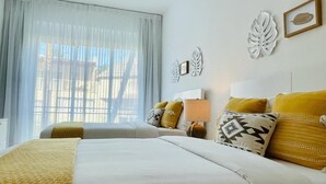 Een hotelkamer met twee bedden, een groot raam met dunne gordijnen en decoratieve muurkunst.