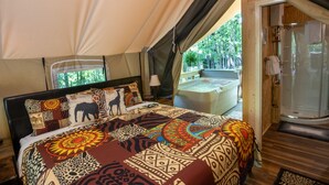 Een slaapkamer in tentstijl met een bed, een douchegedeelte en uitzicht op groen buiten.
