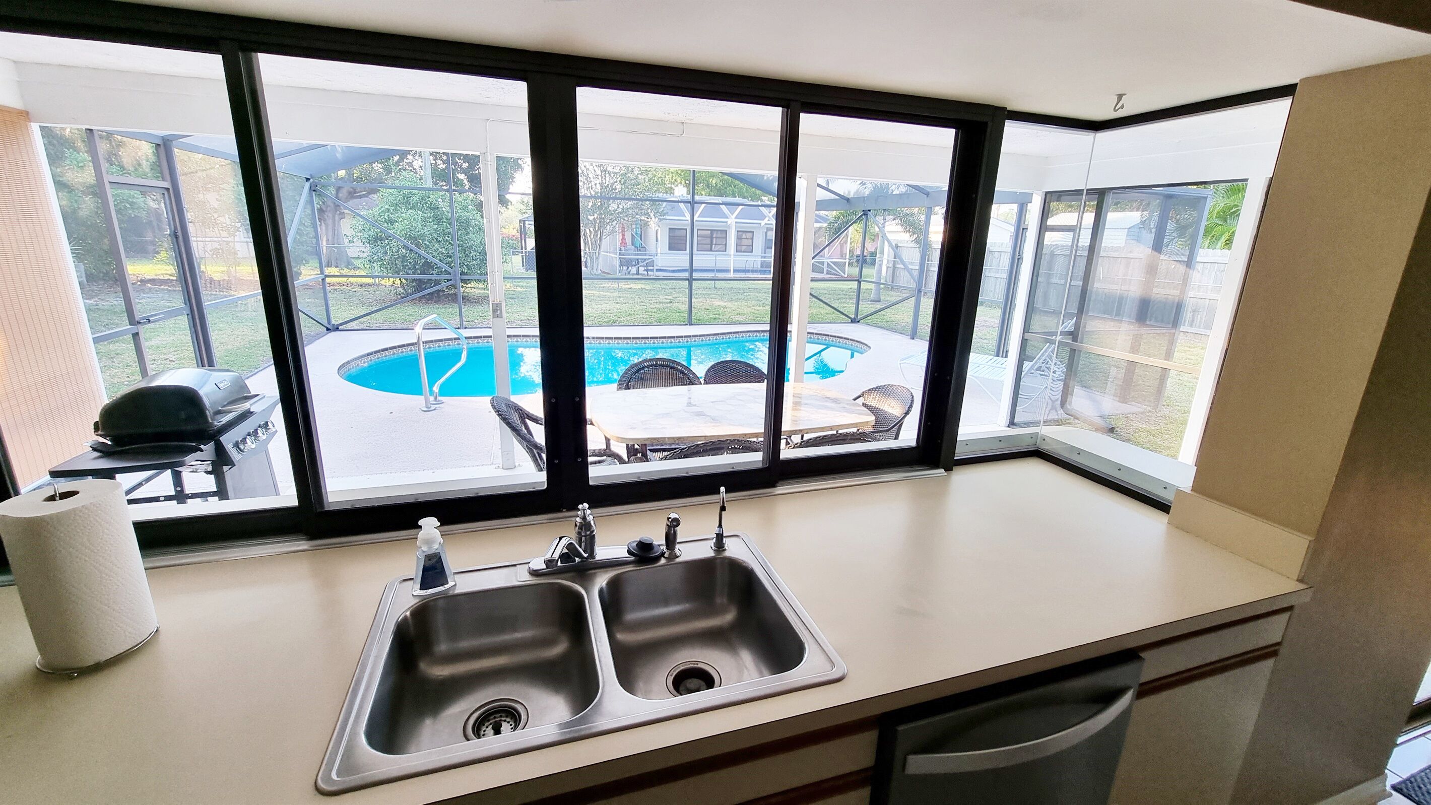A kitchen with a large window overlooking a backyard with a pool and outdoor furniture.