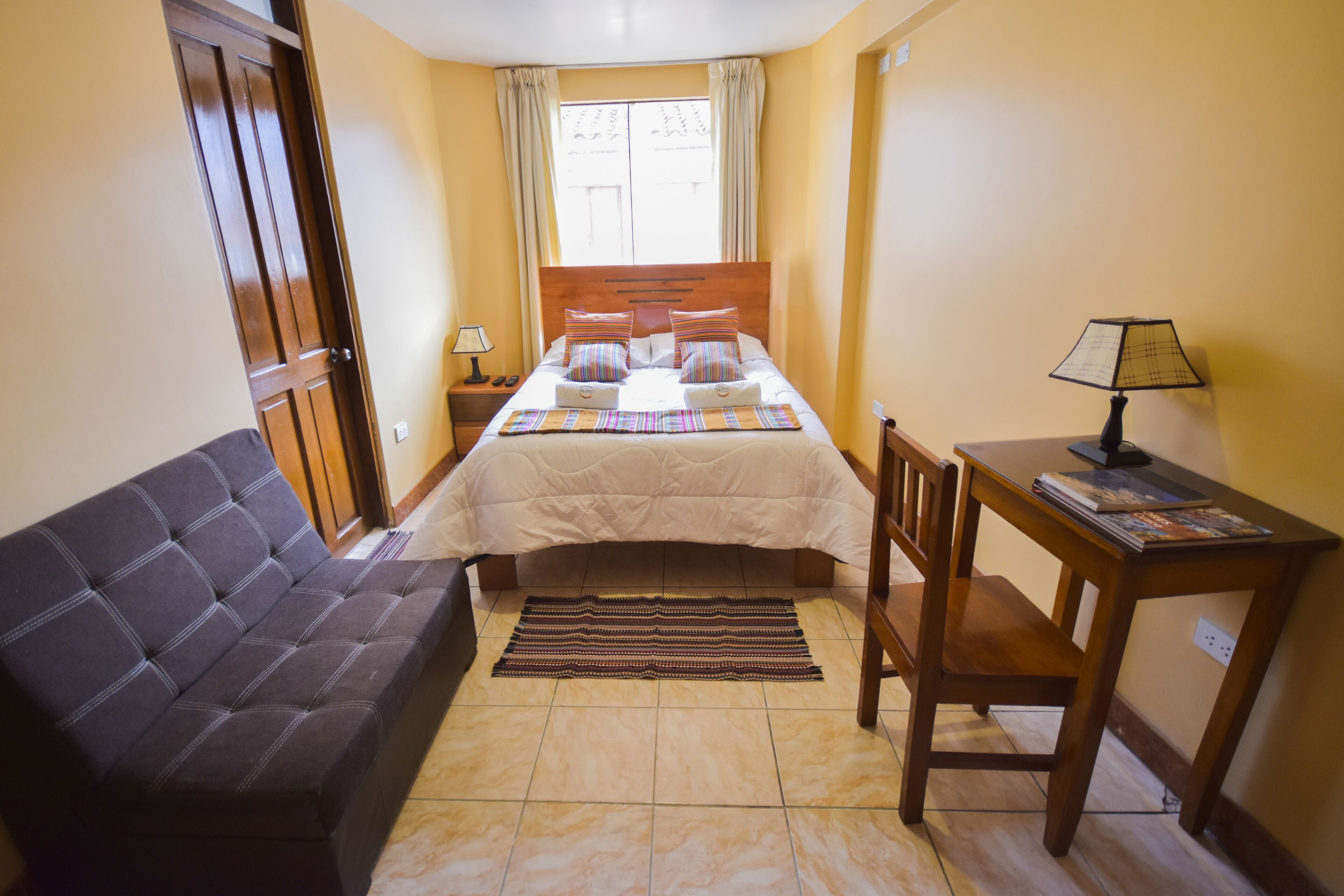 A bedroom with a bed, a sofa, a desk, and a lamp.