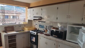 A kitchen with white cabinets, a gas stove, a microwave, and a window with a view of a town. - Friendly and comfortable apartment in Cusco (cusco)