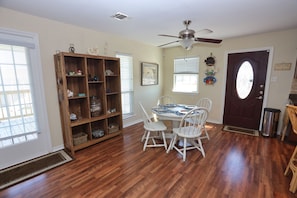 A dining area with a wooden table and white chairs, a ceiling fan, and a door with a window.