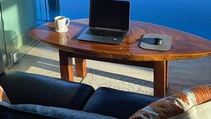 Een balkon met een laptop, een beker en een smartphone op een houten tafel, met uitzicht op de kust.