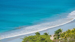 Een strand met helder turquoise water, een zandstrand en palmbomen.