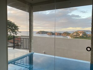 Un balcon avec une porte vitrée, une piscine et une vue sur la mer et les bâtiments éloignés.