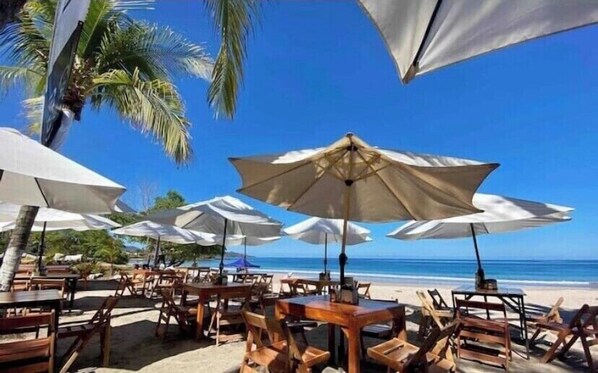 Un restaurant situé en bord de mer, avec une terrasse, des parasols et une vue sur l’océan.