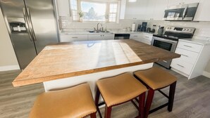 Moderni keittiö, jossa on keskeinen saareke, ruostumattomasta teräksestä valmistetut kodinkoneet ja puiset jakkarat.