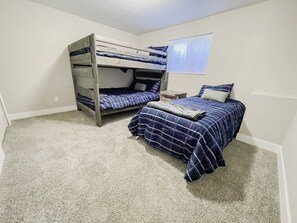 A bedroom with bunk beds, a single bed, a nightstand, and a window with curtains.
