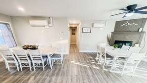 Moderni ruokailutila, jossa on puinen pöytä ja valkoiset tuolit, kattotuuletin ja takka.