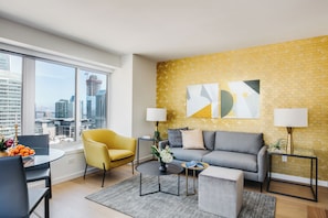 A modern living room with a city view, a yellow armchair, a grey sofa, and a round coffee table. - Stunning One Bedroom in Luxury SoMa Building (San Francisco)