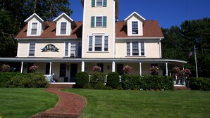 A two-story building with a central tower, a covered porch, and a brick pathway leading to the entrance. - Waterfront Smith Cove Lake House includes dock (Gilford)
