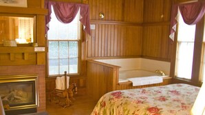 A room with a wooden interior, a fireplace, a bed with floral bedding, and a bathtub. - Waterfront Smith Cove Lake House includes dock (Gilford)
