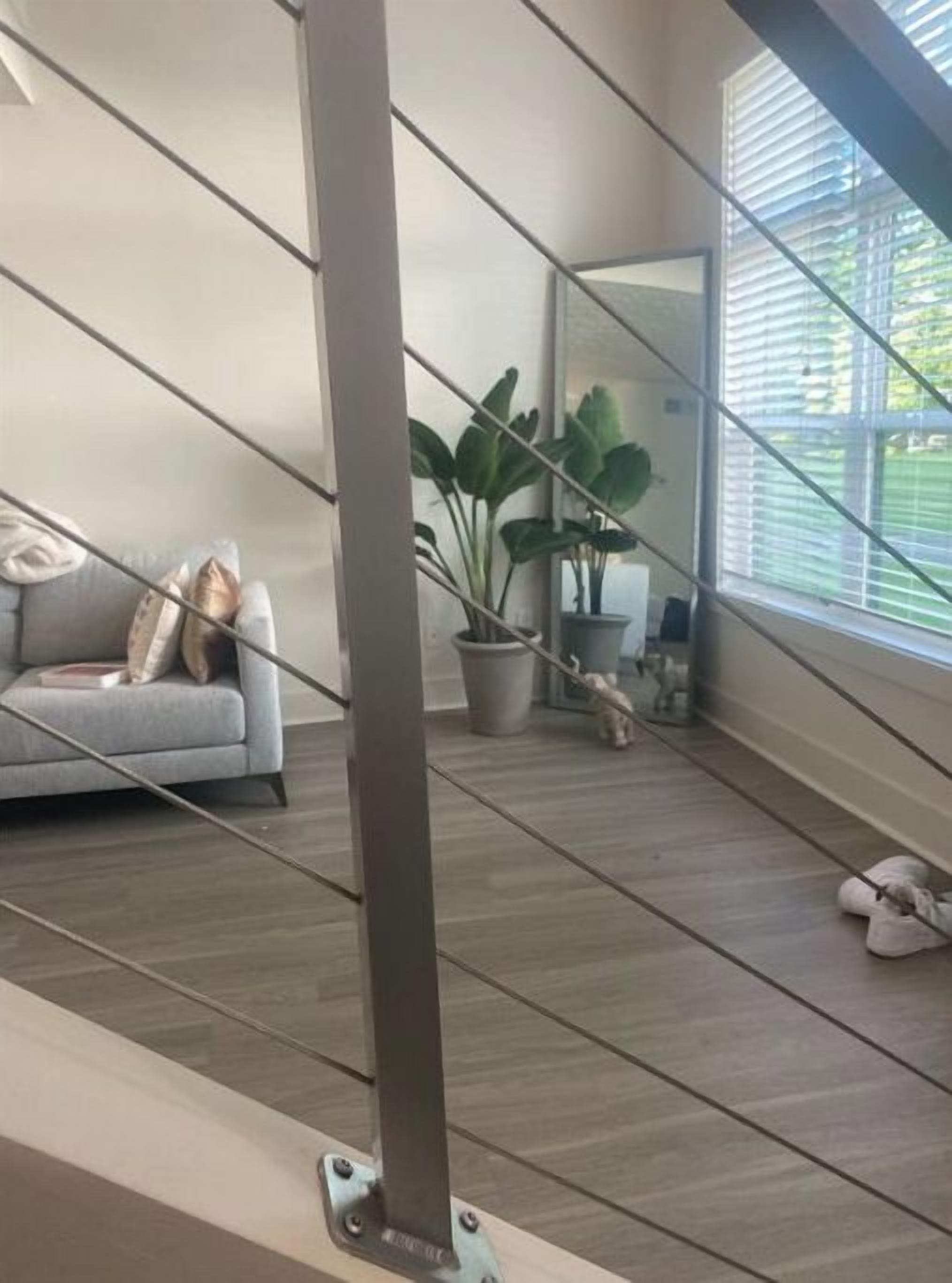 A modern interior with a grey sofa, a potted plant, and a large window with blinds.