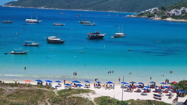 A beach with boats, umbrellas, and people. - Arraial Praia dos Anjos Residence Club (Arraial do Cabo)