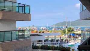 A modern building with multiple balconies overlooking a marina with boats and a pool area. - Arraial Praia dos Anjos Residence Club (Arraial do Cabo)