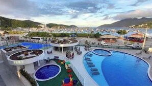 A cruise ship deck with multiple swimming pools, lounge areas, and a view of the coastline. - Arraial Praia dos Anjos Residence Club (Arraial do Cabo)