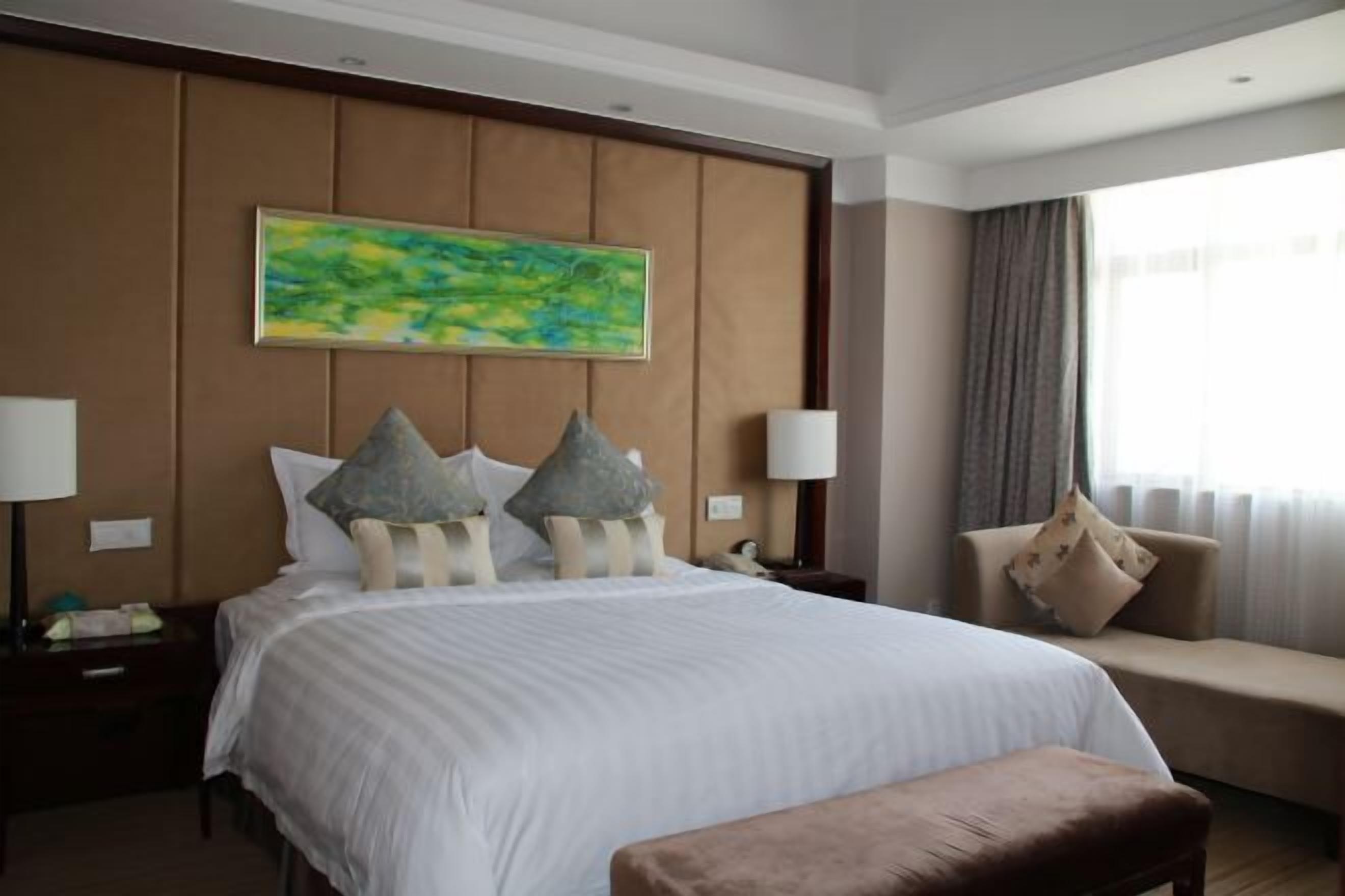 A hotel room with a large bed, a sofa, a bench, and a painting on the wall.