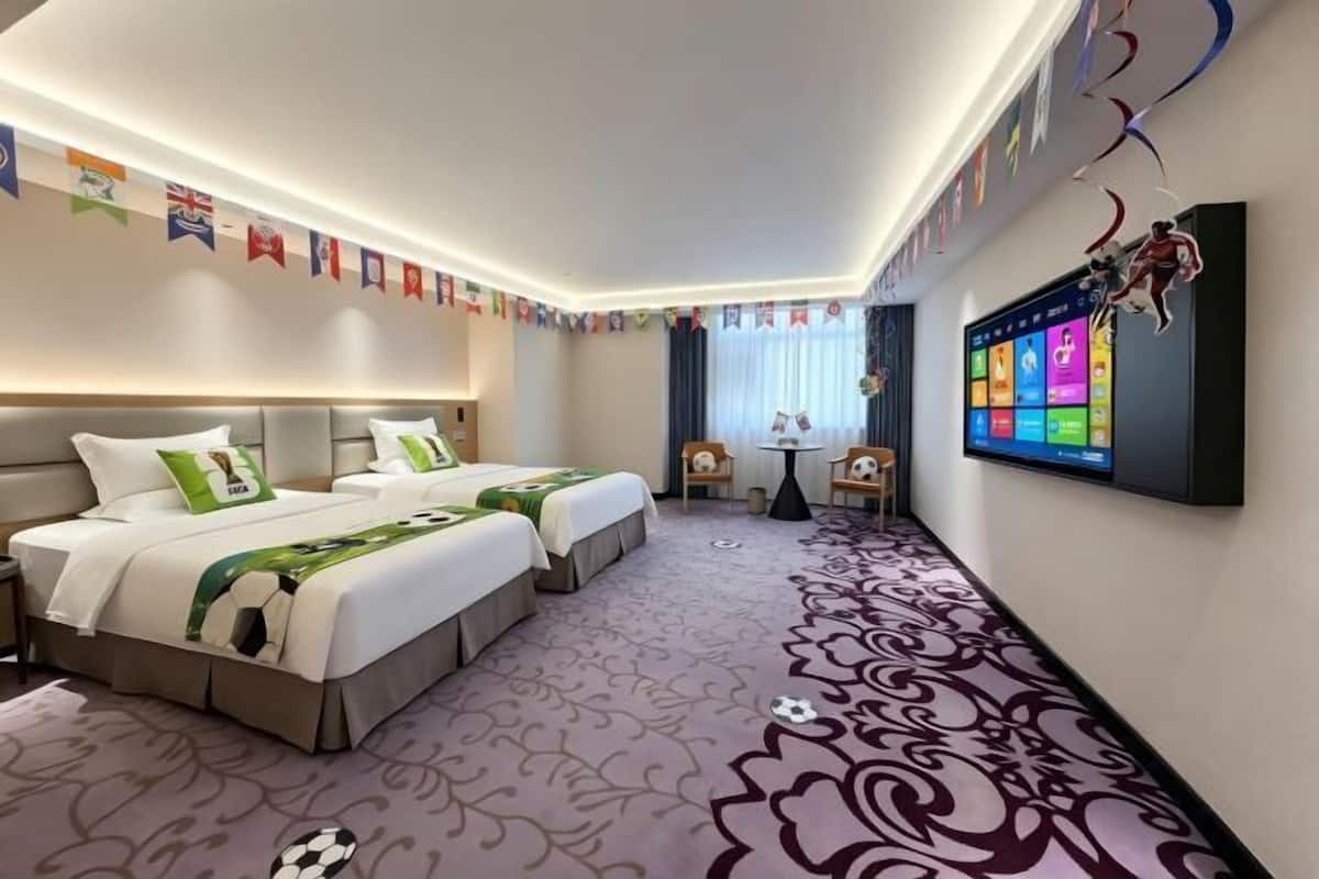 A hotel room with two beds, a TV, a small table, and a decorative wall.