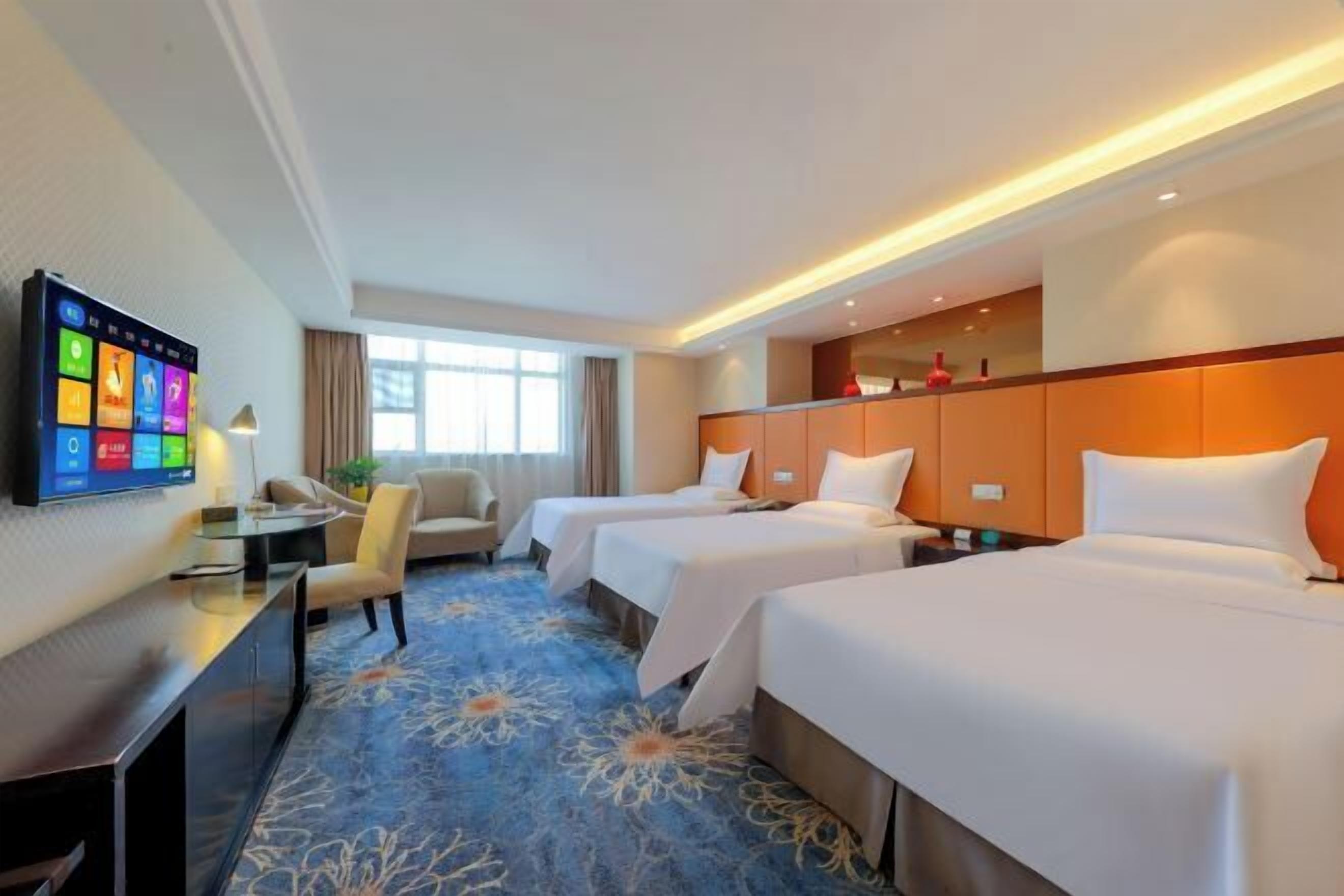 A hotel room with two beds, a TV, a desk, and a window.
