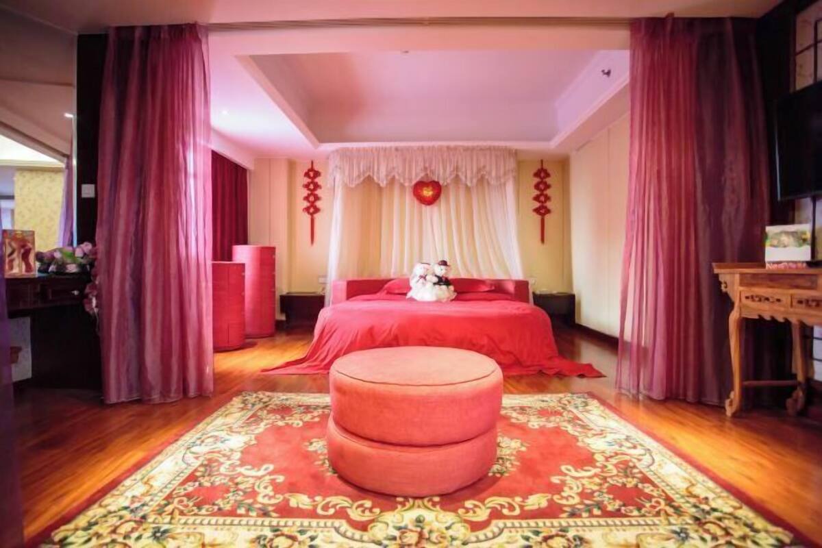 A room with a red bed, a matching ottoman, and a patterned rug.