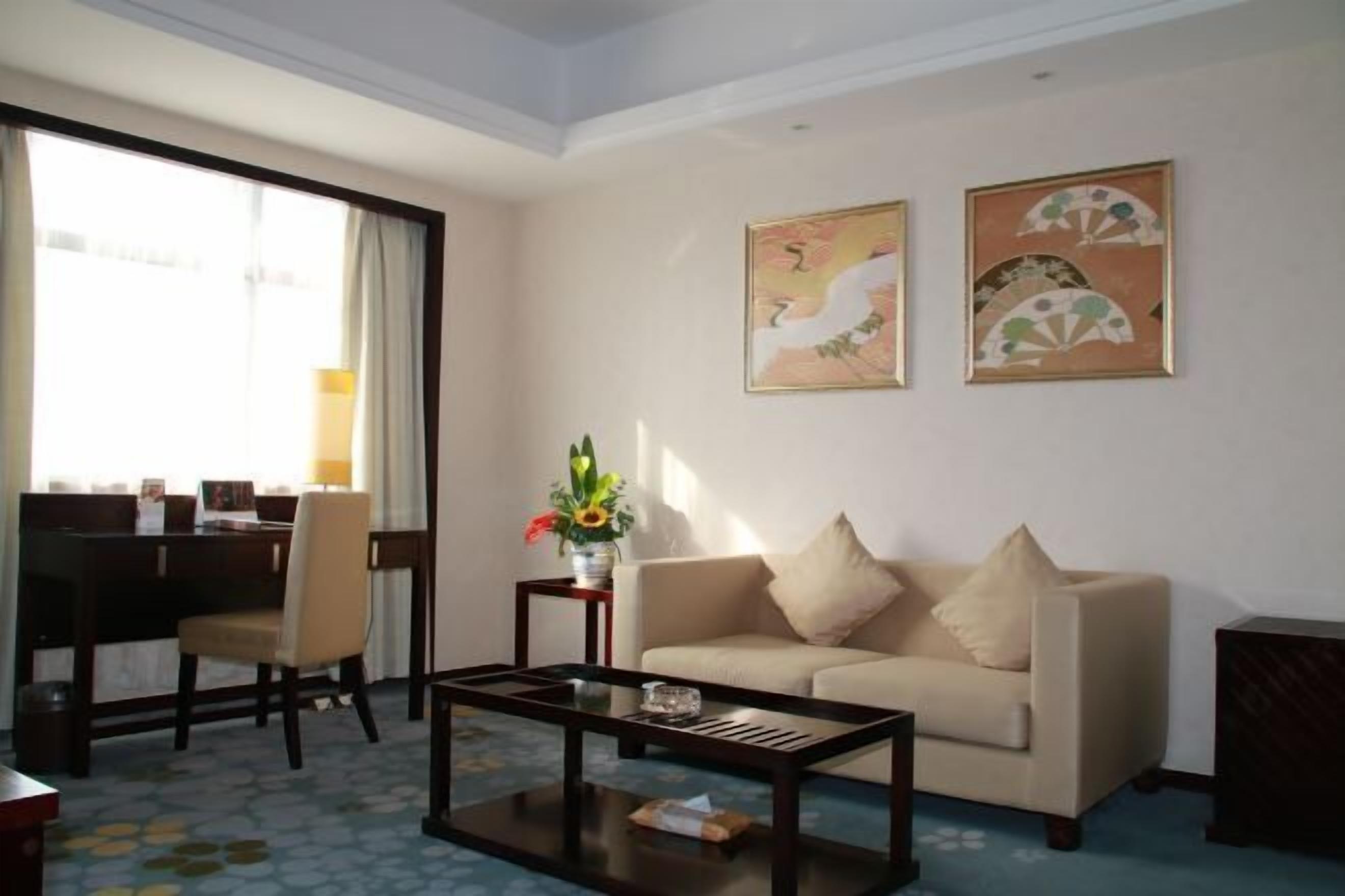 A living room with a sofa, a coffee table, a desk with a chair, and two wall-mounted paintings.