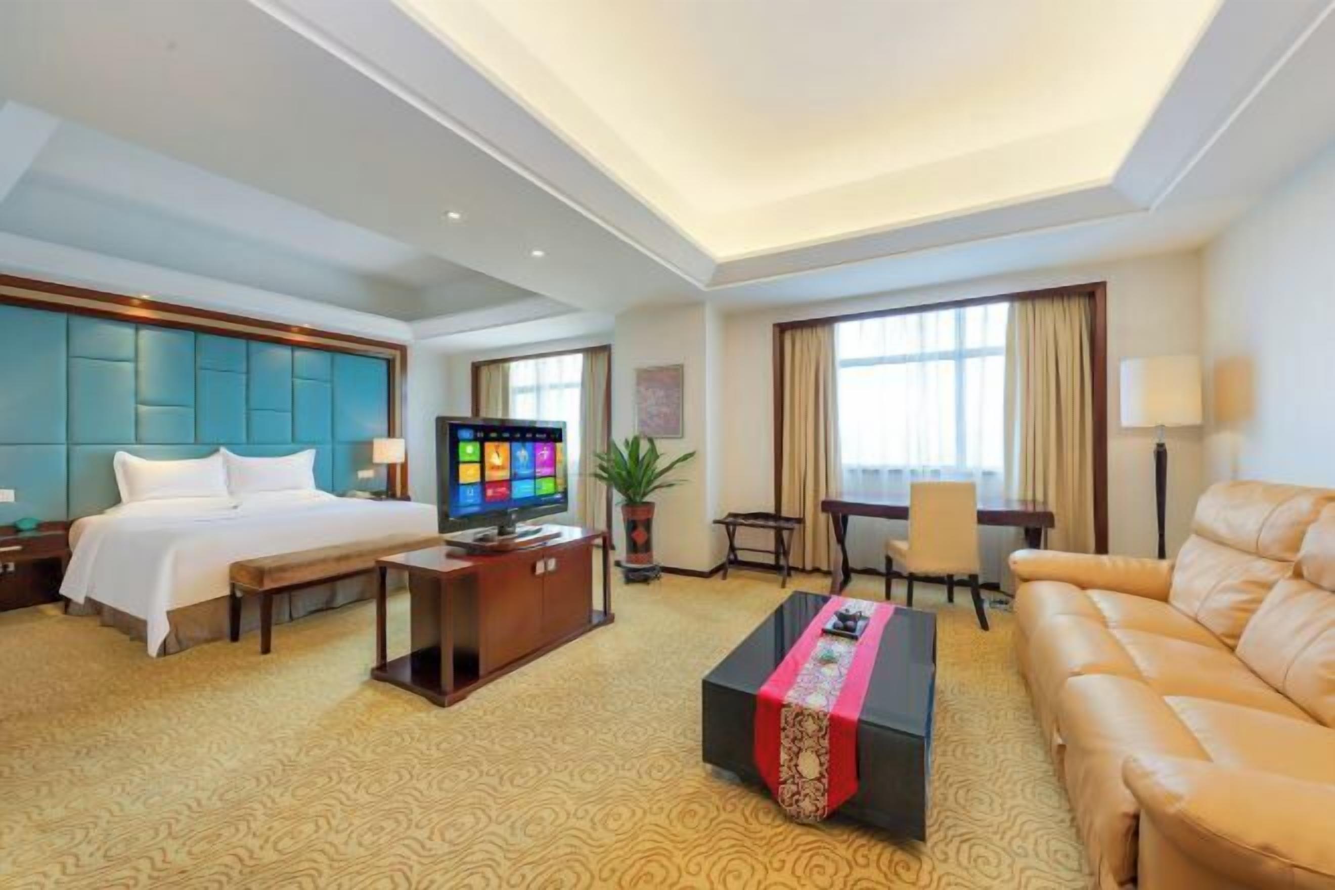Ein Hotelzimmer mit Bett, Fernseher, Schreibtisch, Sofa und Couchtisch.