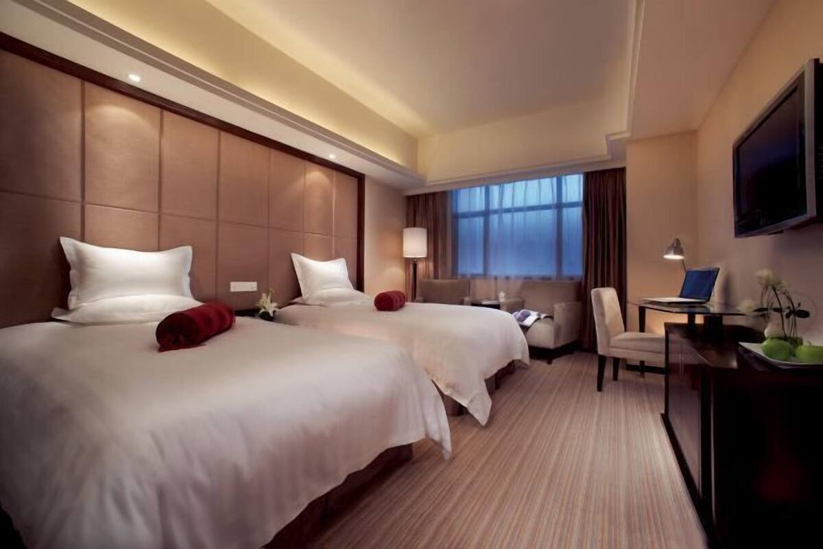 A hotel room with two beds, a desk, a chair, a TV, and a window with curtains.
