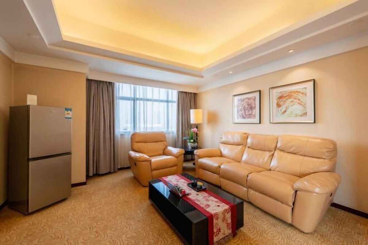 A hotel room with a sofa, a chair, a coffee table, a lamp, and a refrigerator.