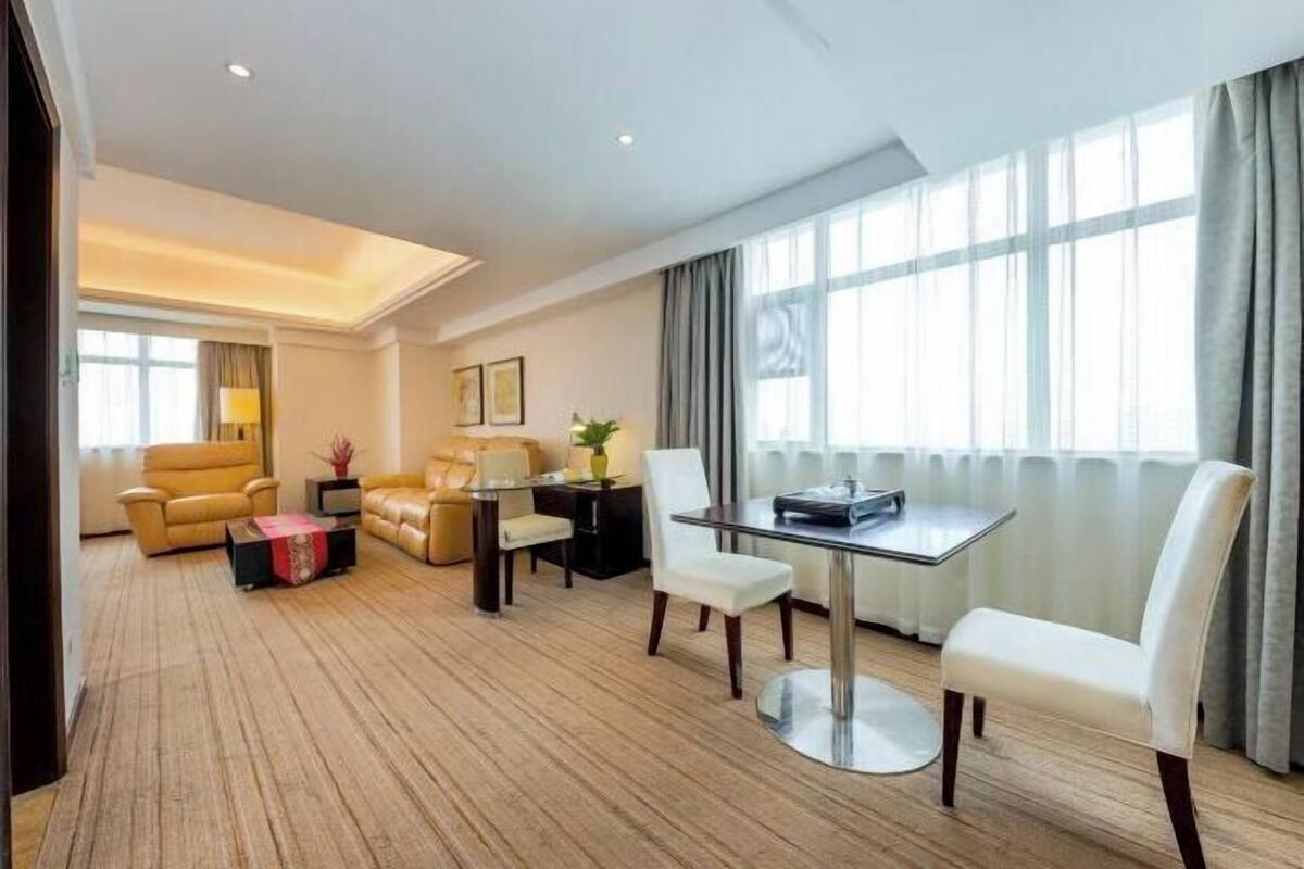 A hotel room with a living area, a dining table with chairs, a sofa, and a TV.