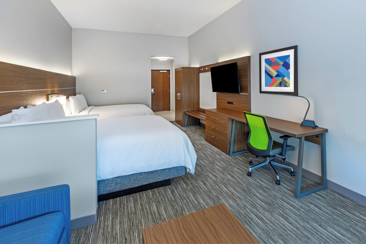 A hotel room with a bed, a desk, a chair, a TV, and a painting on the wall.