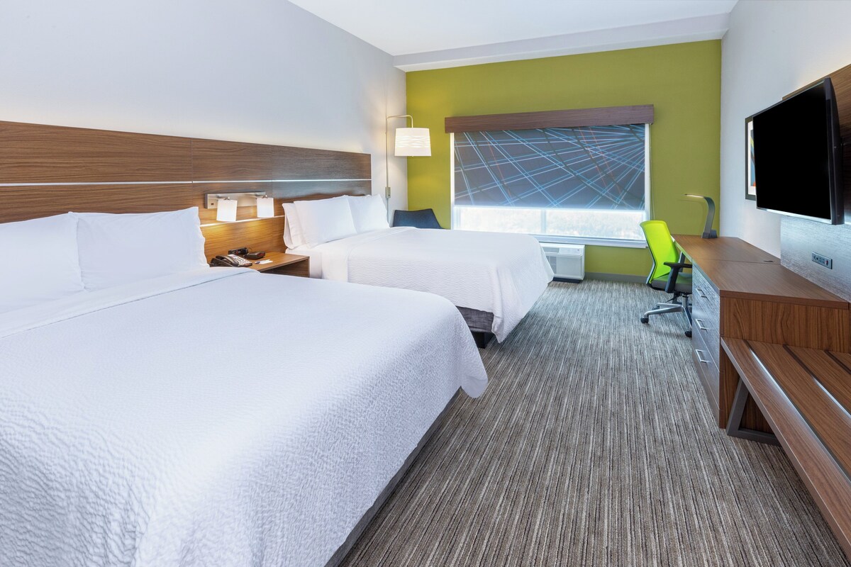 A hotel room with two beds, a desk, a chair, a TV, and a window with a view.