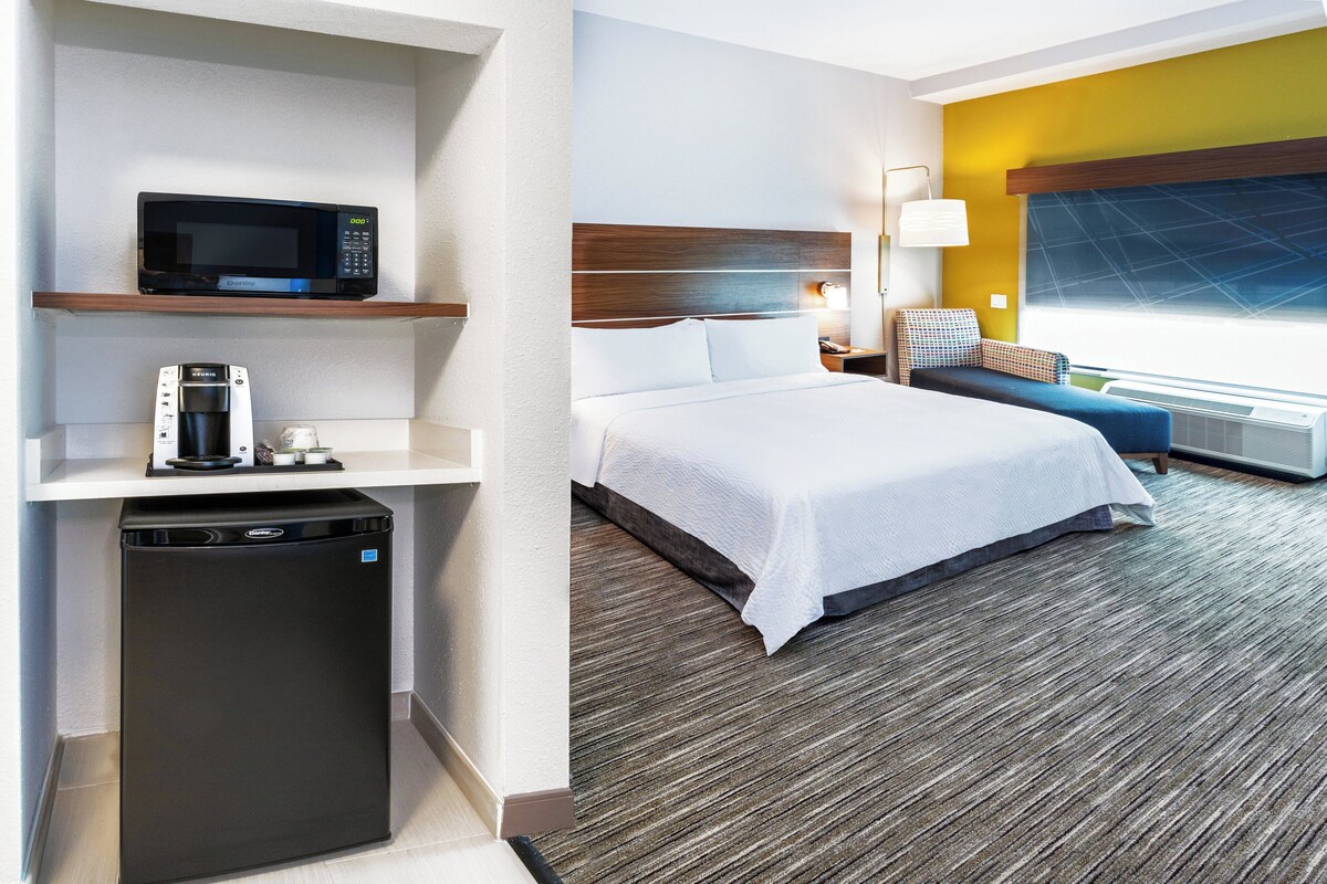 A hotel room with a bed, a microwave, a coffee machine, and a mini-fridge.
