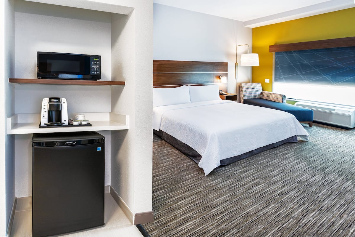 Habitación de hotel con cama, microondas, cafetera y refrigerador pequeño.