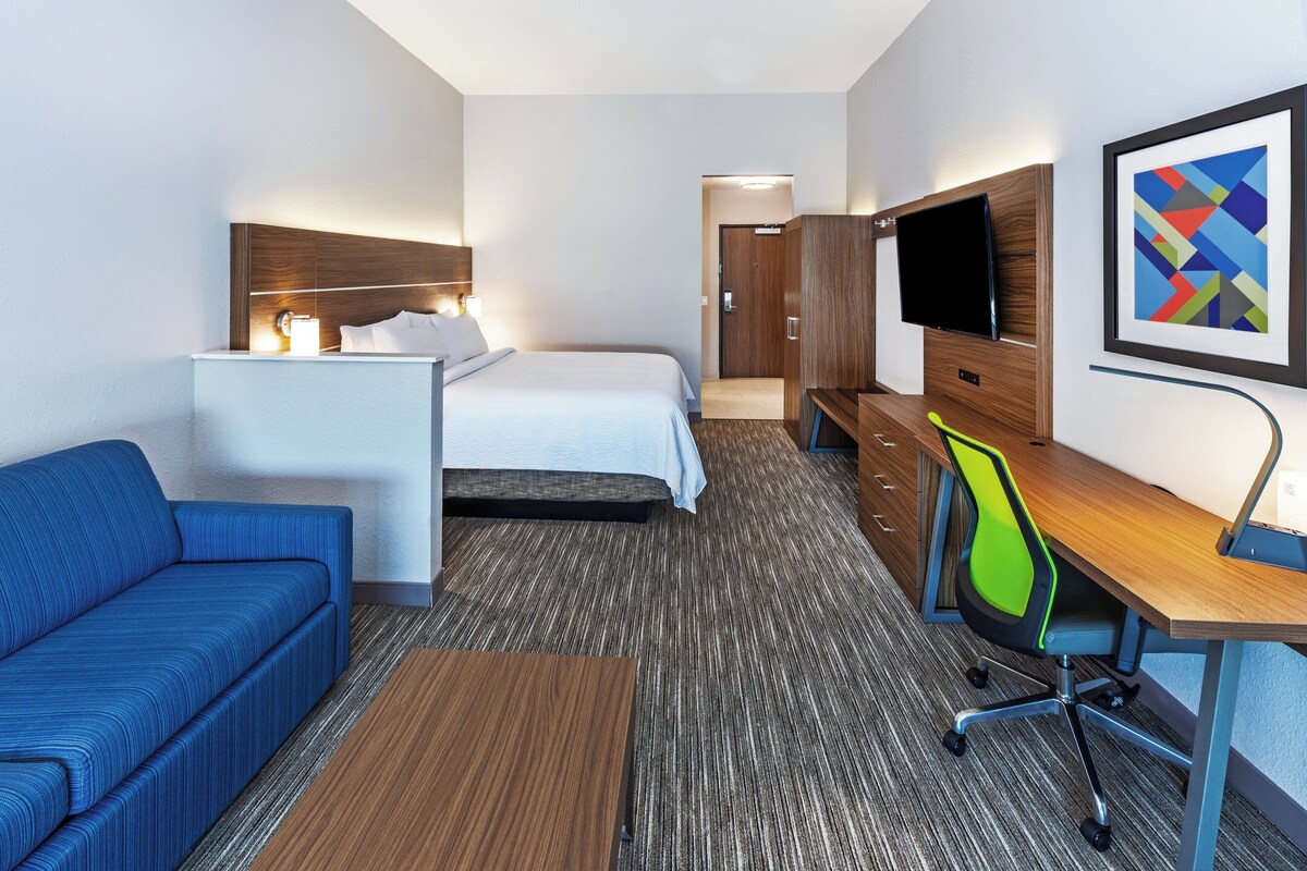 A hotel room with a bed, a desk with a chair, a sofa, and a TV.