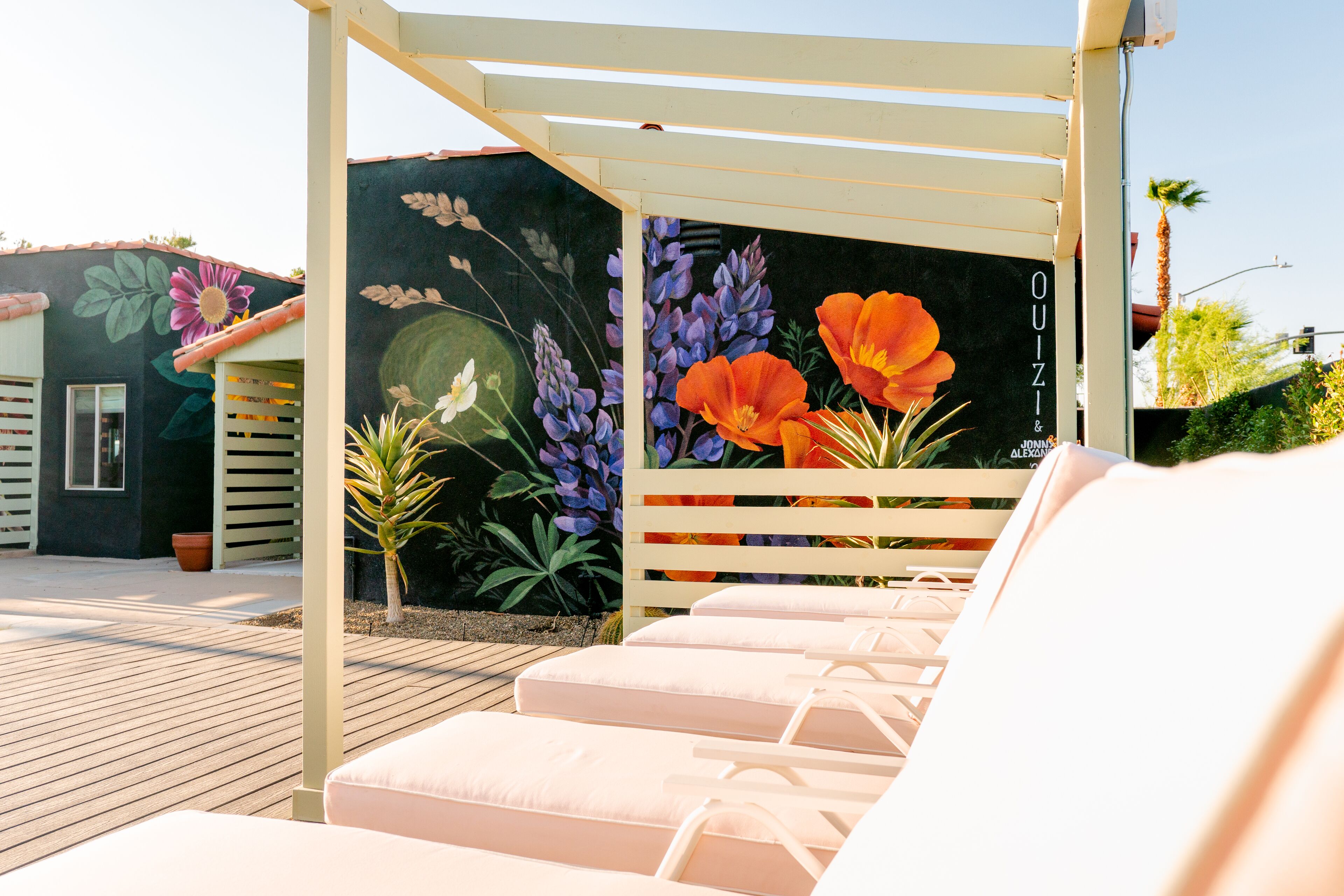 A covered outdoor seating area with lounge chairs and a mural with flowers and text.