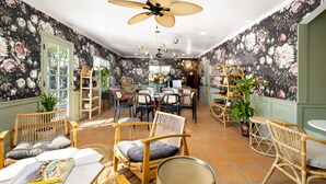 A room with floral wallpaper, wicker furniture, and a ceiling fan. - Fleur Noire Hotel - 21 and Over (Palm Springs)