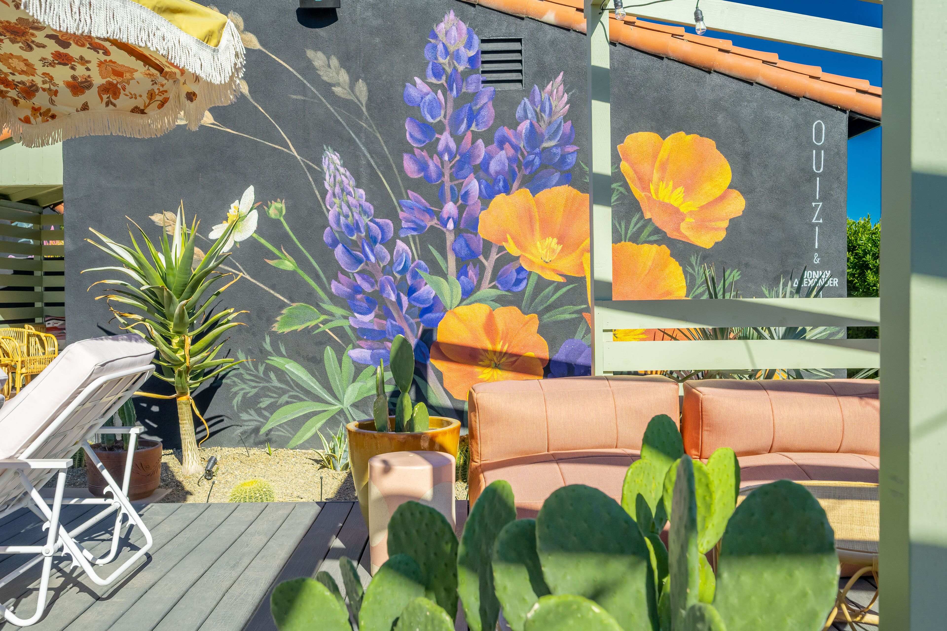 An outdoor seating area with a mural of flowers, a cactus, and a sofa.