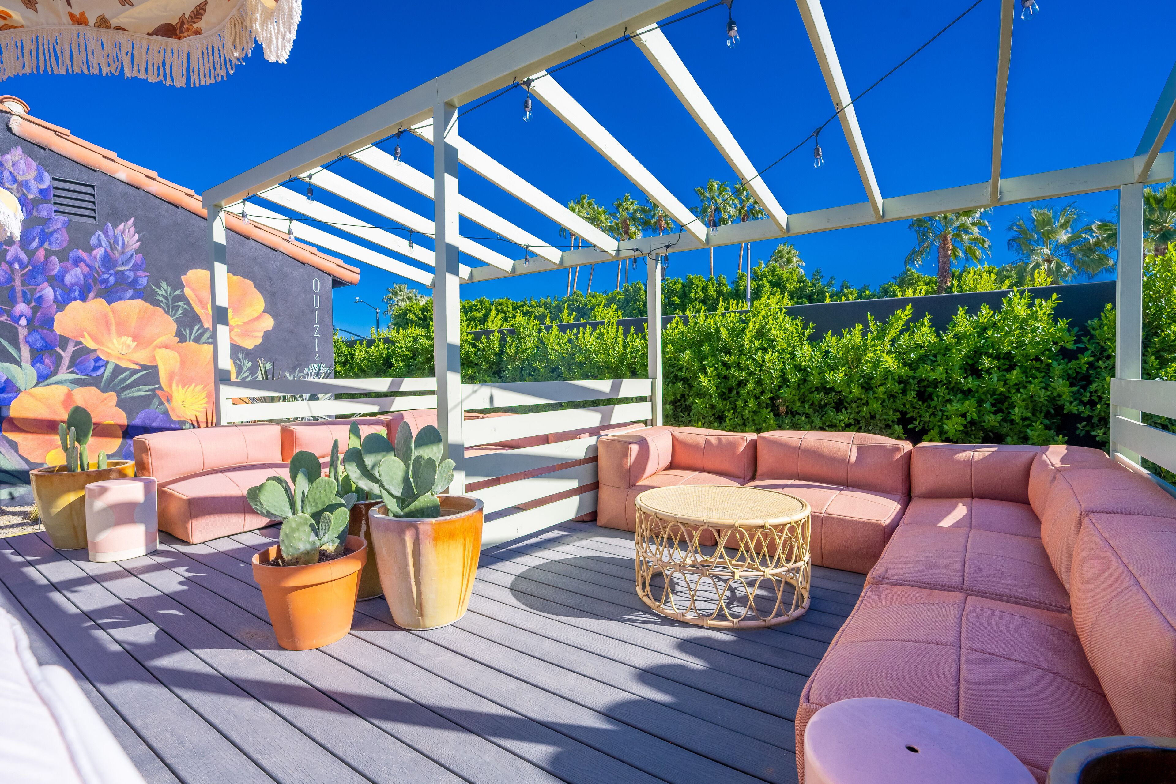 Une terrasse extérieure dotée de sièges confortables, de plantes en pot et d’une fresque représentant des fleurs.