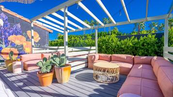 Une terrasse extérieure dotée de sièges confortables, de plantes en pot et d’une fresque représentant des fleurs.