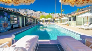 A pool area with lounge chairs and umbrellas, surrounded by buildings with floral murals and a mountain backdrop. - Fleur Noire Hotel - 21 and Over (Palm Springs)