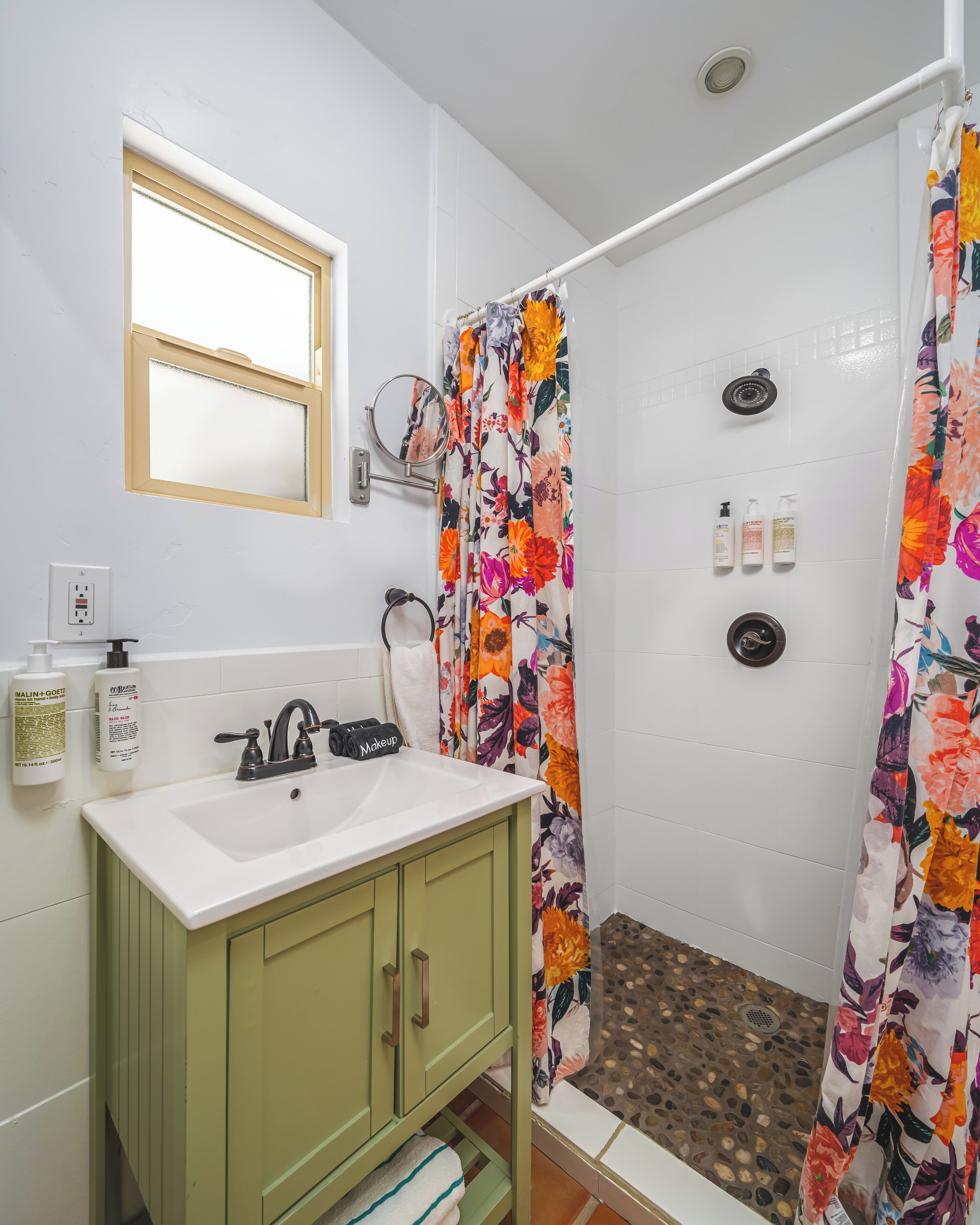 A bathroom with a white sink, green cabinets, a mirror, and a shower with a floral curtain.