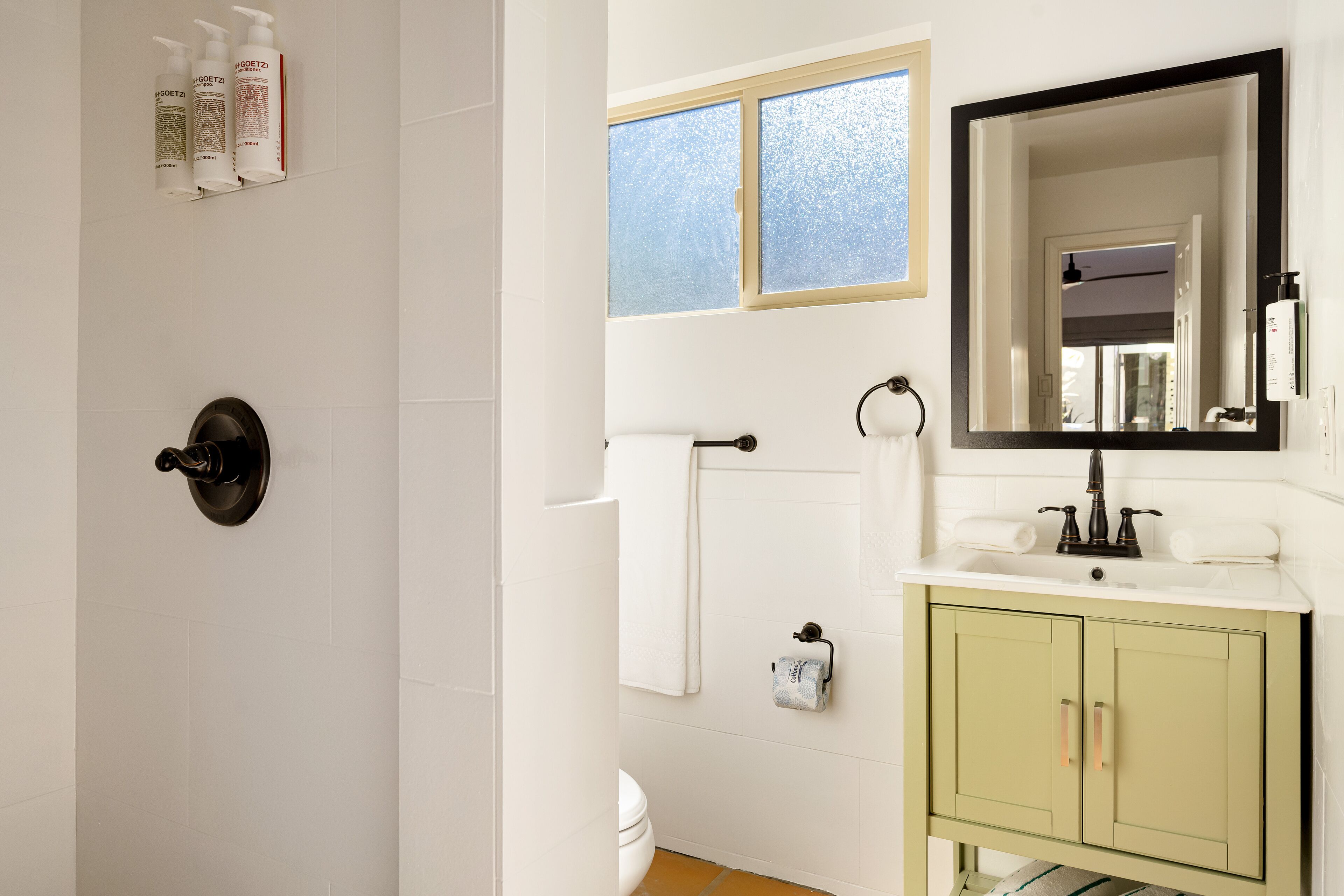 A bathroom with a toilet, sink, mirror, and window.