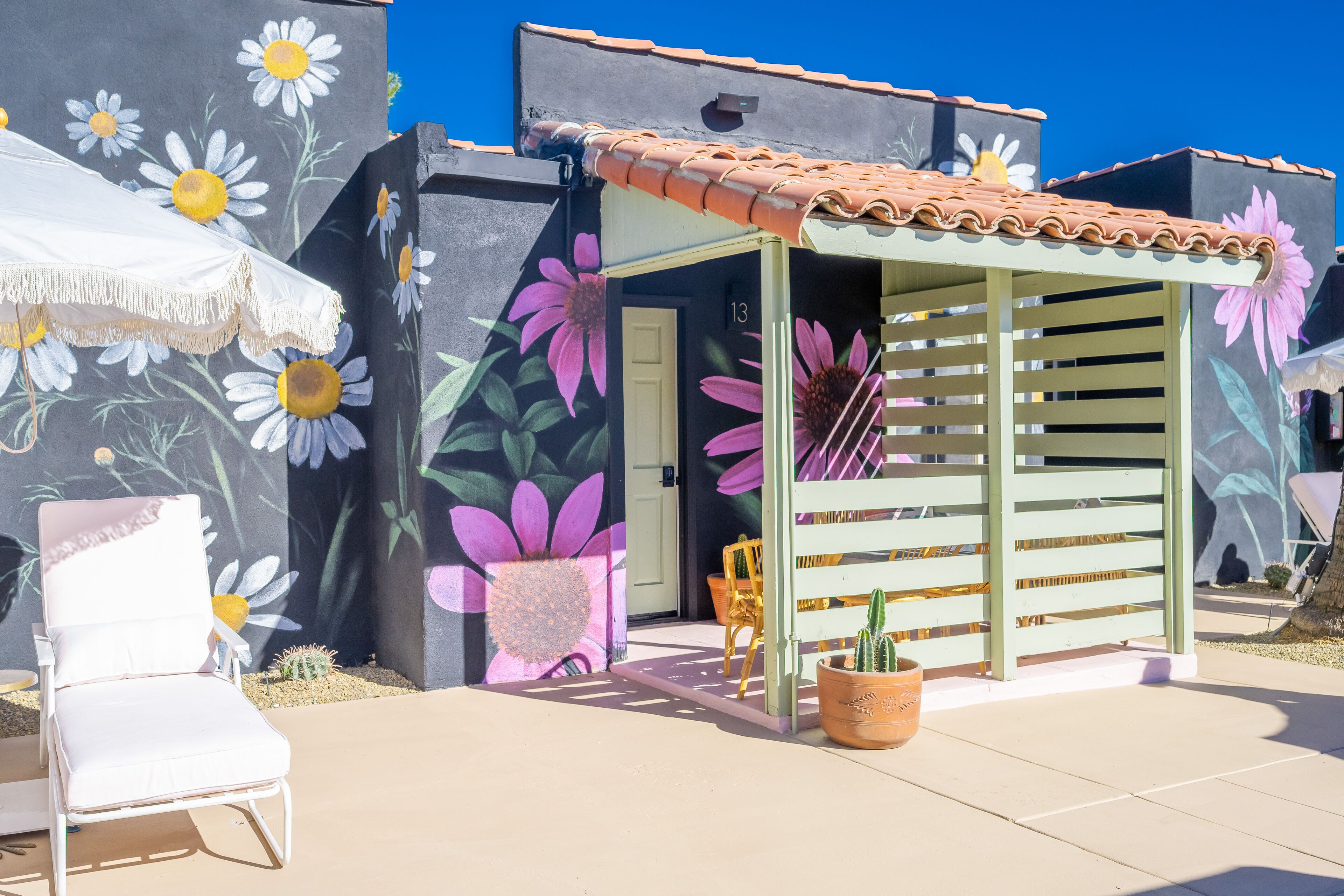 Un edificio con un mural floral vibrante, un pequeño patio cubierto con una silla y una planta de cactus.