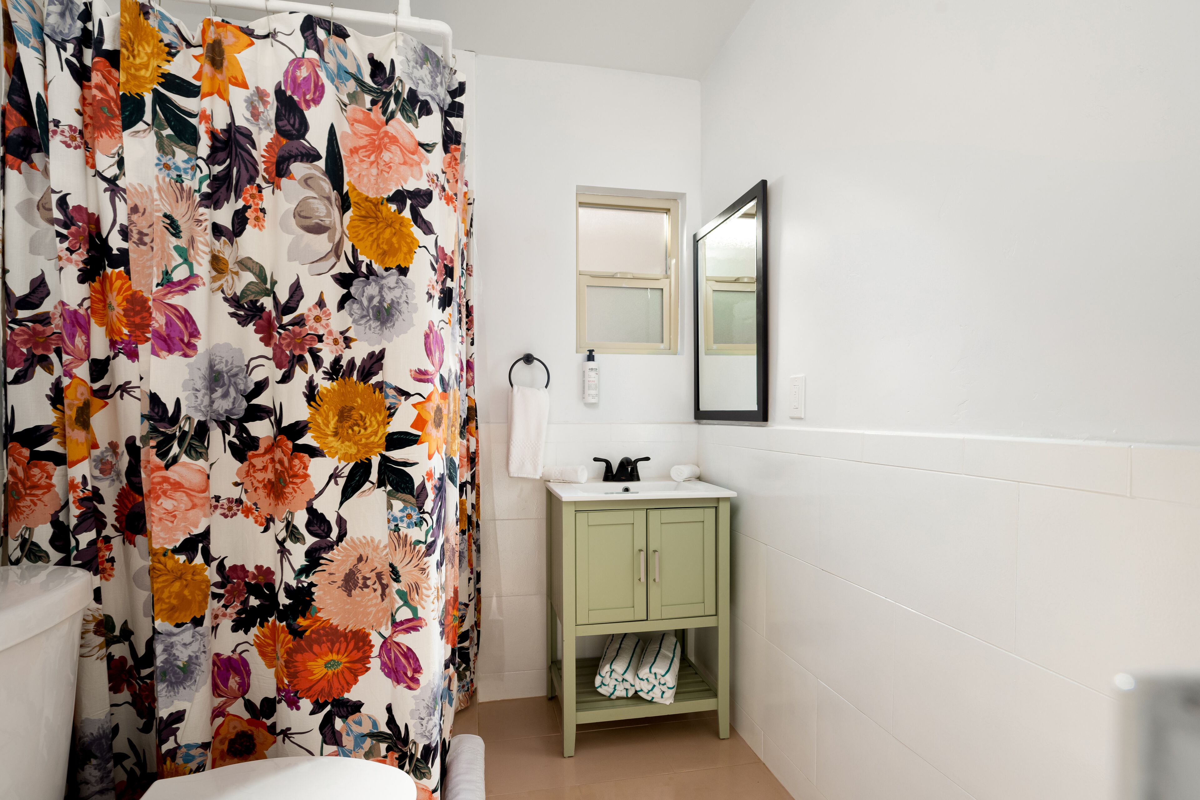A bathroom with a floral shower curtain, a green cabinet with a sink, and a mirror on the wall.