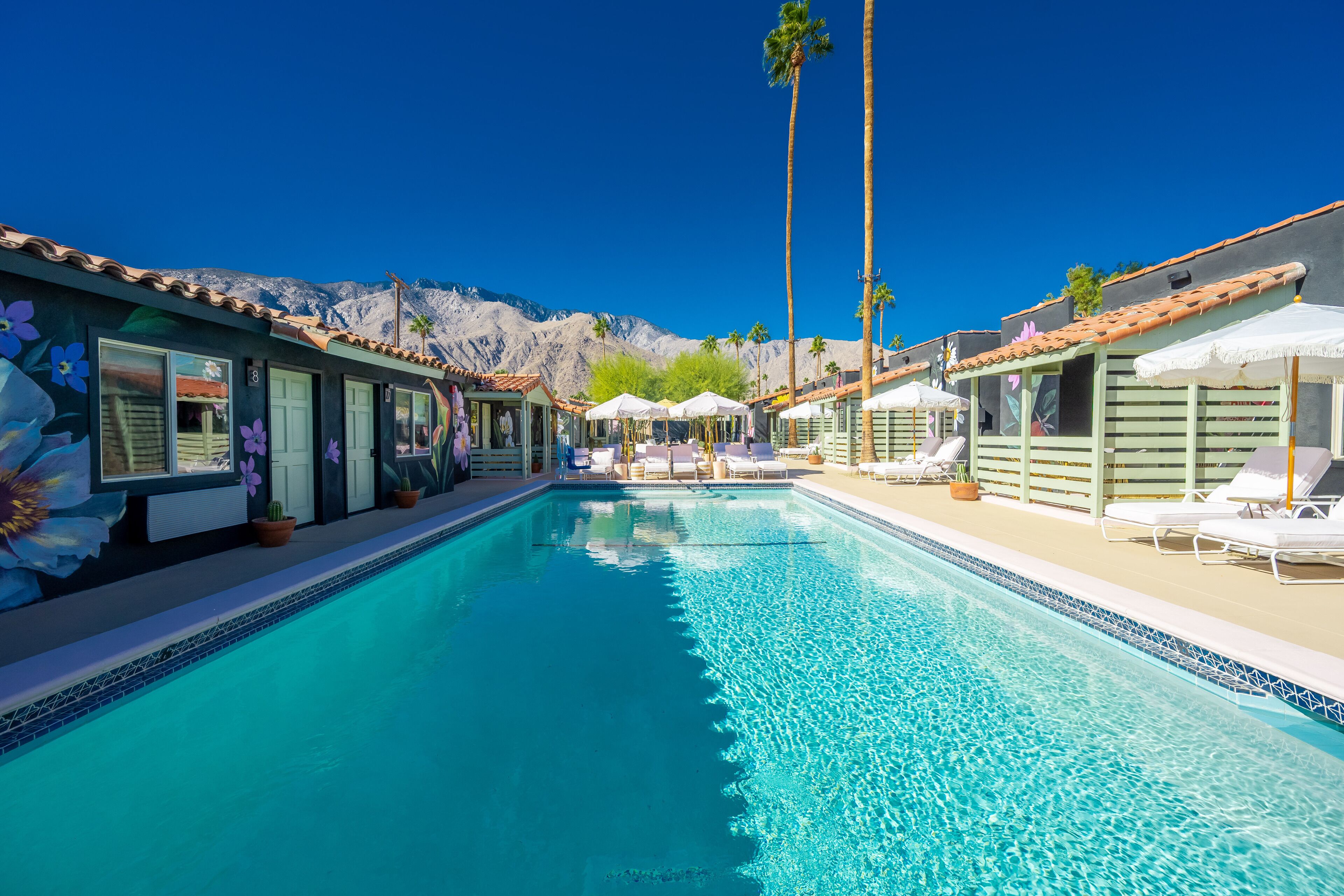 A swimming pool with lounge chairs and umbrellas, surrounded by buildings with a mountain backdrop.